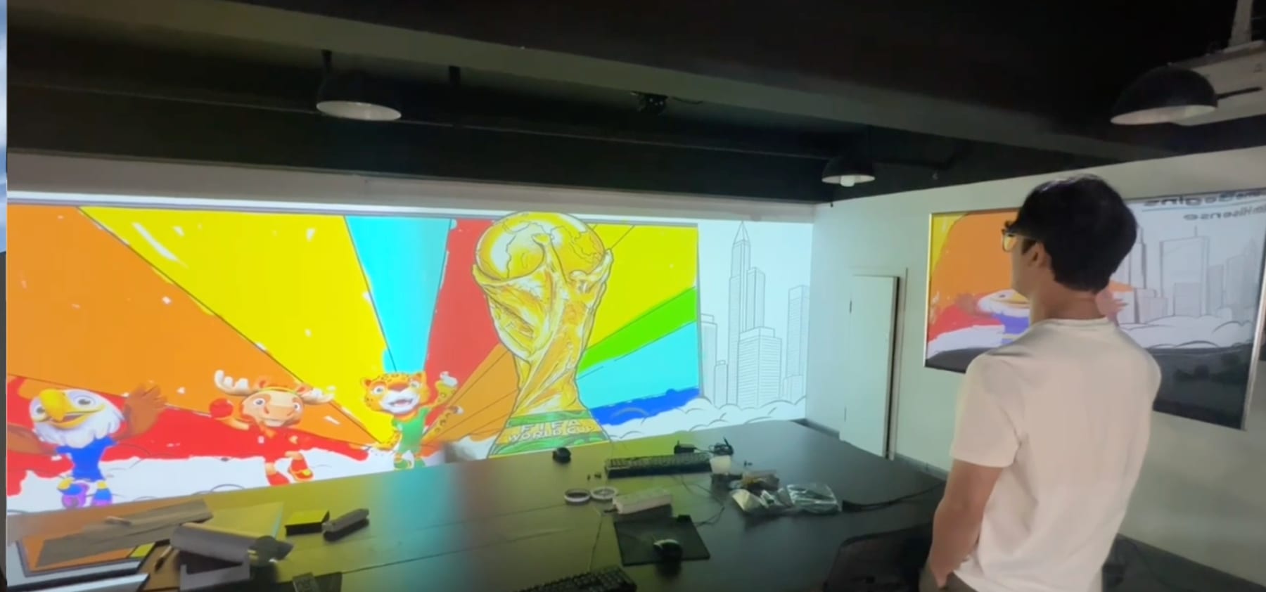 The graffiti wall content under test on a full-width wall in the MLABART facility in China before shipping, with workstations and keyboards along the bench and a second screen mirroring the canvas